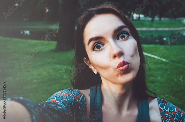 Obraz Pretty girl taking photo selfie and making duck face. Female sending kisses, enjoying self portrait. Herself Instagram concept. Lifestyle  of happy woman looking on camera phone.