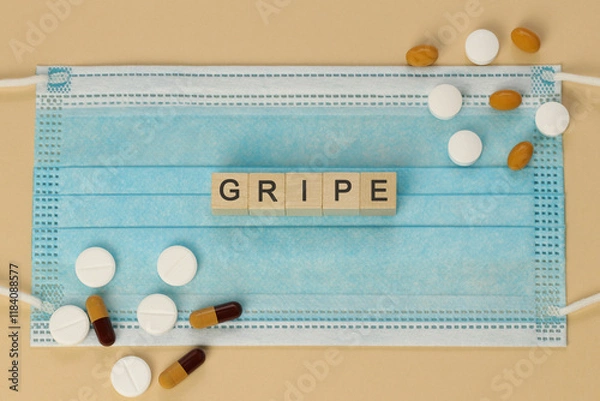 Fototapeta Gripe - influenza in spanish and portuguese, spelled with wooden cubes on a surgical mask, surrounded by pills and capsules.