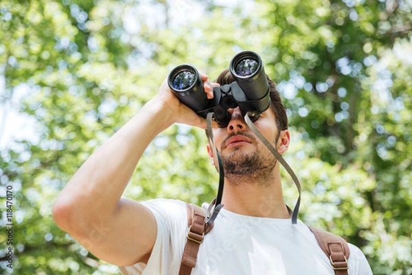 Fototapeta Man with backpack looking through binoculars in forest
