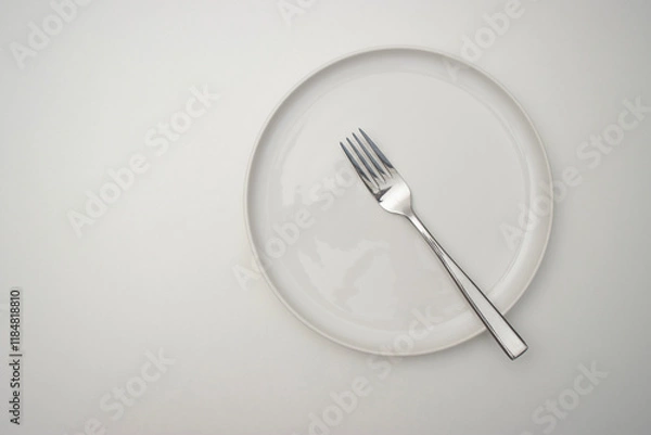 Fototapeta White plate on a white table. There is a fork on the plate. Top view, copy space