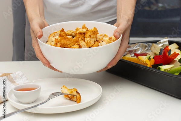Fototapeta Female hands put chicken bowl on table. Fried chicken pieces and vegetables. Close-up, copy space