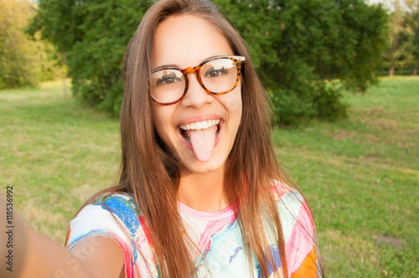 Fototapeta Close up portrait of a young attractive woman holding a smartphone and taking a selfie