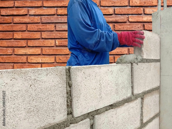 Fototapeta Construction worker is installing concrete wall with cement block and plaster on brick background at the construction area.