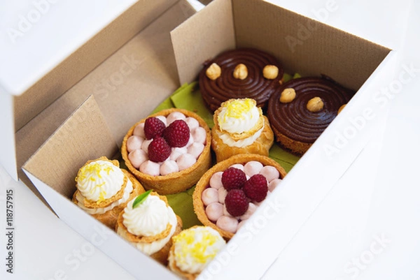 Obraz Desserts in the white paper delivery box. Freshly baked tarts and eclairs in the box. Desserts package.