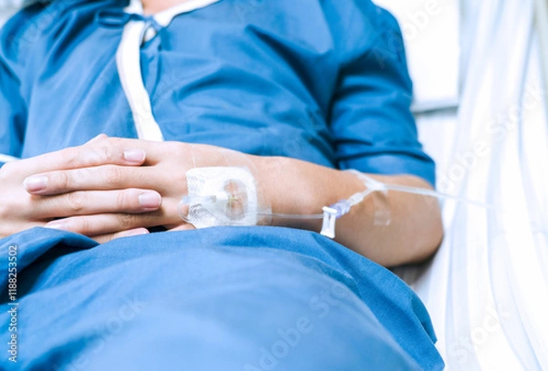 Obraz The saline tube on the left hand of the patient is giving the saline solution that lies in the hospital bed