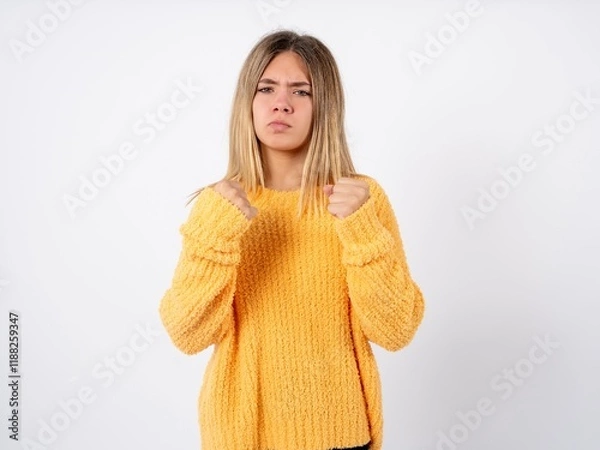 Fototapeta Beautiful caucasian teen girl wearing orange sweater crosses arms and points at different sides hesitates between two items or variants. Needs help with decision