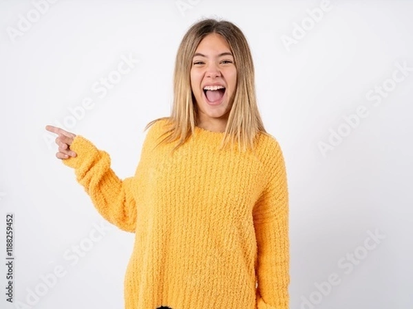 Fototapeta Beautiful caucasian teen girl wearing orange sweater points at copy space and advertises something, advices best price.