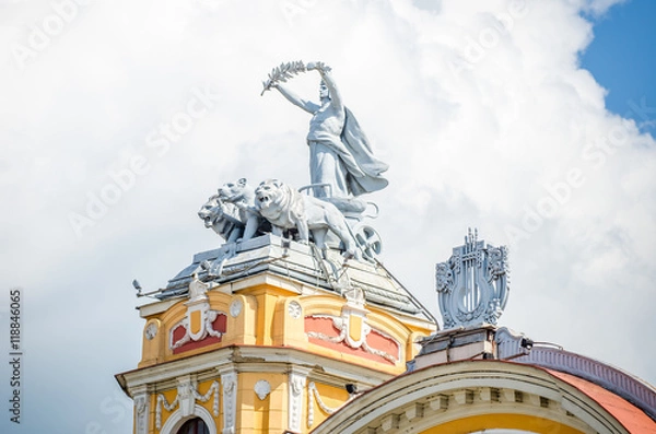 Obraz Statue on allegorical car pulled by lions on a tower at the Cuj-Napoca National Theatre and Opera House in the Transylvania region of Romania. A baroque rococo building in a close view