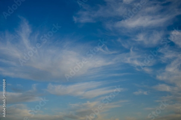 Fototapeta Striking cloud patterns gracefully drift across the deep blue sky at sunset
