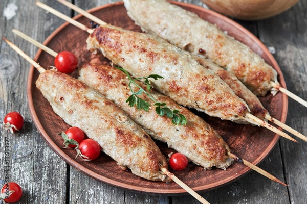 Fototapeta Grilled kebabs on wooden skewers and fresh vegetables on a plate close-up. horizontal