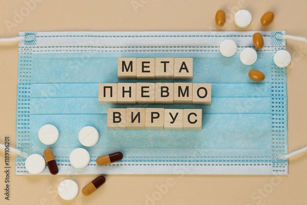 Fototapeta Метапневмовирус - metapneumovirus in Russian, spelled with wooden cubes on a surgical mask, surrounded by pills.   Written in Cyrillic also in languages such as Macedonian, Bashkir, Kyrgyz, Tatar.