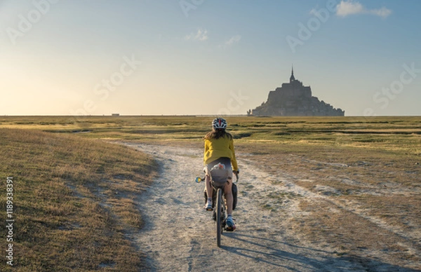 Obraz Bike and adventure in Mont Saint Michel. Female traveler pedals through rural area, in the background is the famous Mount Saint Michel.