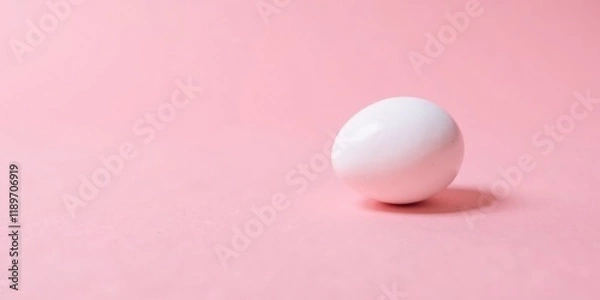 Fototapeta A solitary white egg rests gently on a soft pink background, a minimalist composition ideal for springtime themes or product showcasing.