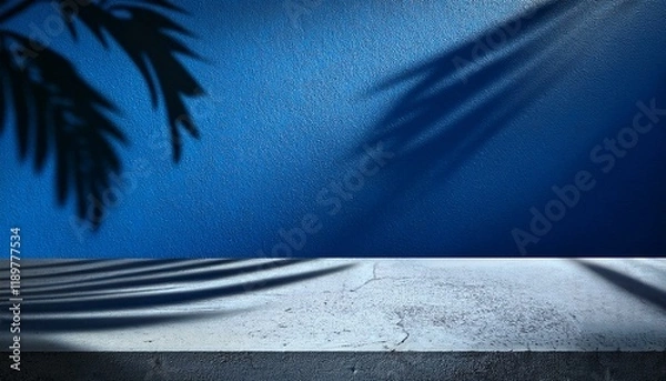 Fototapeta Shadowy palm fronds cast an ethereal glow on a cool concrete surface against a deep blue wall.