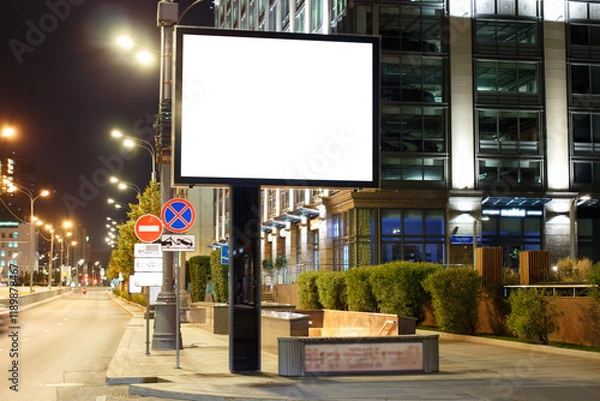 Fototapeta Large horizontal billboard in the night city. Building with multi-level parking, clean road. Mock-up.