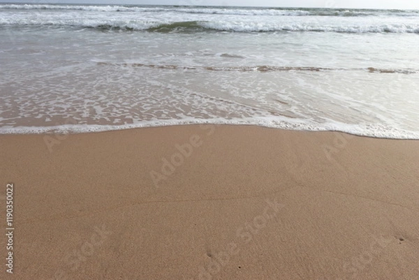 Fototapeta waves crashing on shore of sandy beach on a cloudy day