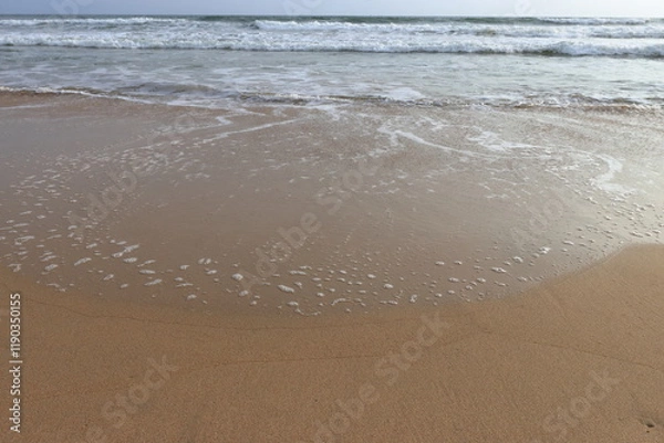 Fototapeta waves crashing on shore of sandy beach on a cloudy day