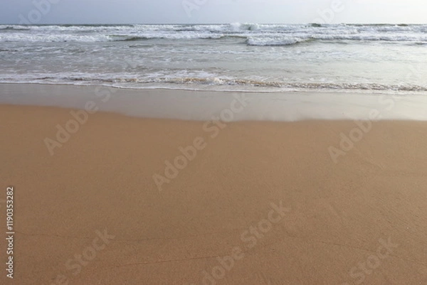 Fototapeta waves crashing on shore of sandy beach on a cloudy day