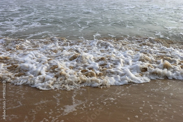 Fototapeta Soothing waves crashing on shore of sandy beach on a cloudy Day
