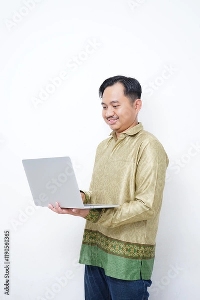Obraz Adult Asian man wearing batik smiling while using his laptop - Indonesia men