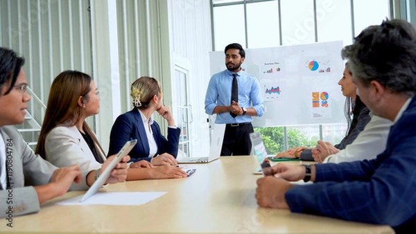 Fototapeta Young indian business manager standing and presenting to multiracial group of diversity colleagues in front of white board in meeting at boardroom in office . leader