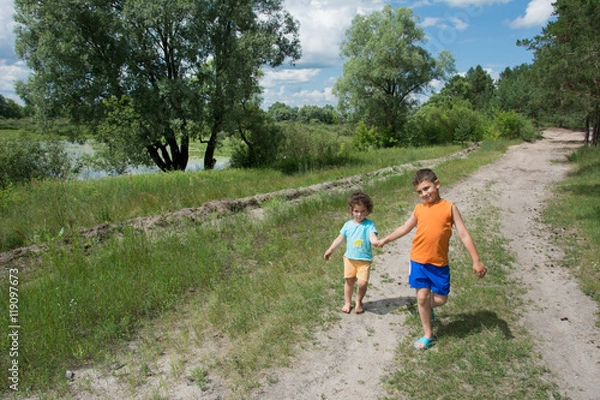 Fototapeta In the forest on the road bright sunny day go a little boy and g