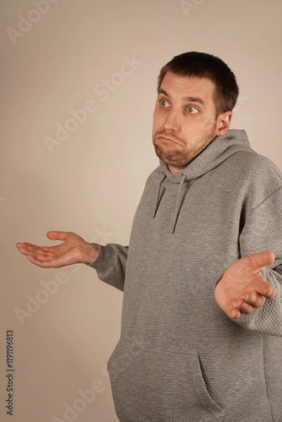 Fototapeta With hands extended outward, a man shrugs, appearing confused. The open palms symbolize his lack of understanding about the situation. His body language reflects uncertainty and wonder.