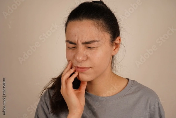 Fototapeta Her body language reflects physical discomfort. The moment is a genuine depiction of personal unease. The woman clutches her gum with a pained expression, capturing the sensation of a toothache.