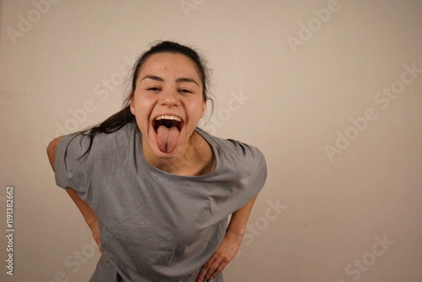 Fototapeta With a playful expression, the girl sticks her tongue out towards the camera in a silly gesture. Her face is full of fun, capturing a light and humorous moment. It is a fun and playful reaction.
