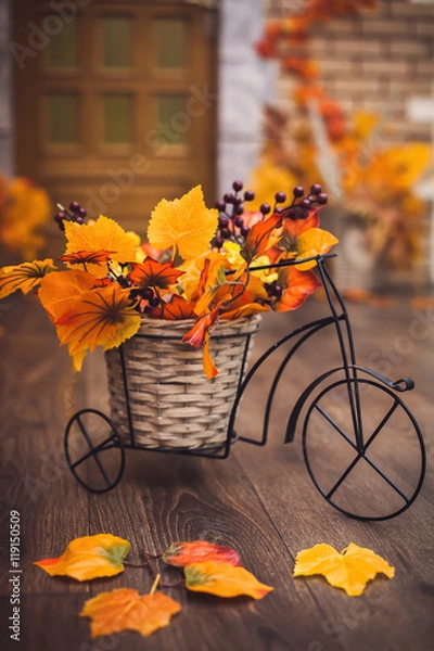 Obraz Small decorative bicycle with basket filled with yellow autumn leaves and grapes berries on the wooden floor.