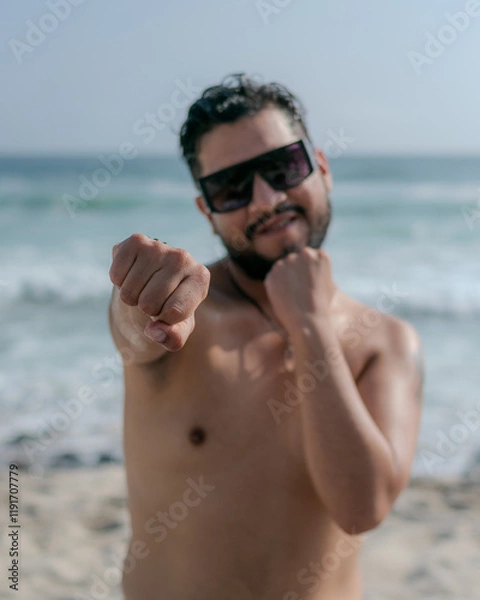 Fototapeta male person with beard and sunglasses doing exercises on the beach with bare torso 