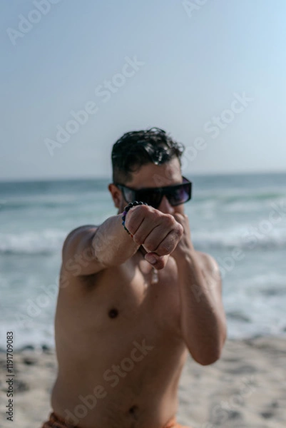 Fototapeta male person with beard and sunglasses doing exercises on the beach with bare torso 