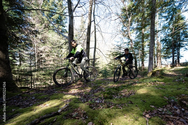 Fototapeta Two cyclists take a break on a lush, mossy trail amidst tall trees. Sunlight filters through the canopy, creating a peaceful atmosphere.