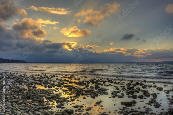 Obraz Sonnenuntergang am Chiemsee mit Steinen am Strand und Wolken am Horizont