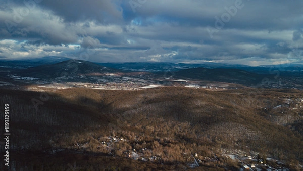Fototapeta A serene aerial capture of rolling hills covered with dense, leafless forests, illustrating the natural tranquility of late autumn or early winter.