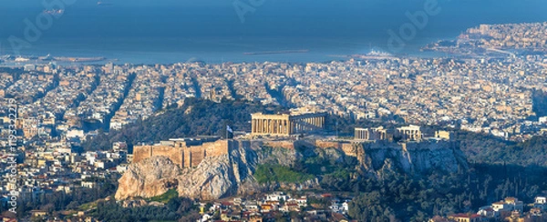 Fototapeta A panoramic view of Athens, Greece, featuring the Acropolis with the Parthenon temple, surrounded by the dense cityscape and the Aegean Sea in the background.