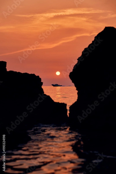 Fototapeta Sun setting over rocks on a beach, reflecting in the water