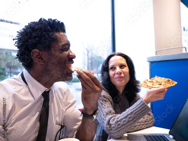 Fototapeta Two colleagues sharing pizza in a casual setting during a lunch break, promoting teamwork, relaxation, and office camaraderie.