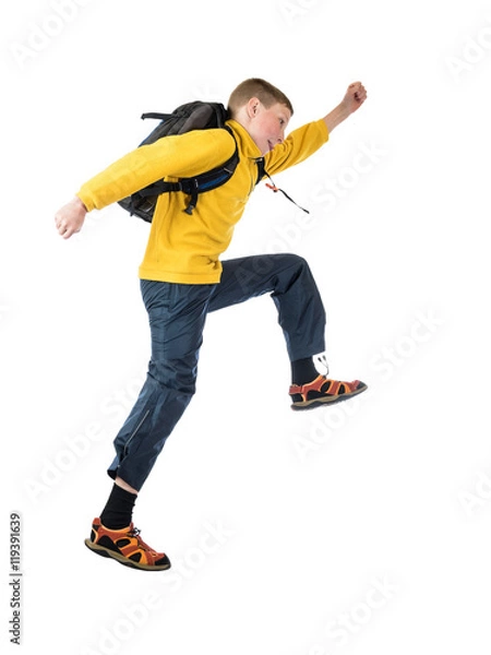 Fototapeta Young red-haired boy in a yellow jacket and a backpack boy jumping with arms outstretched on a white background