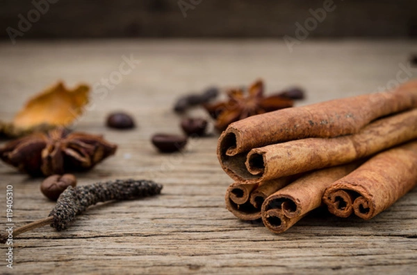 Fototapeta Cinnamon sticks, star anise turmeric and coffee grains on old rustic background, seasoning ingredients for cooking or baking.
