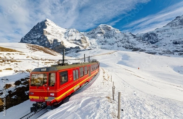 Fototapeta On a sunny winter day, tourists ride on a cogwheel train from Jungfraujoch (Top of Europe) to Kleine Scheidegg on the snowy hillside with Eiger and Monch in background, in Berner Oberland, Switzerland