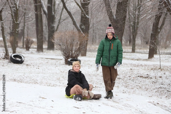 Fototapeta Children are walking, hiking,, sledding and playing in a snowy park. Winter fun and outdoor activities with kids