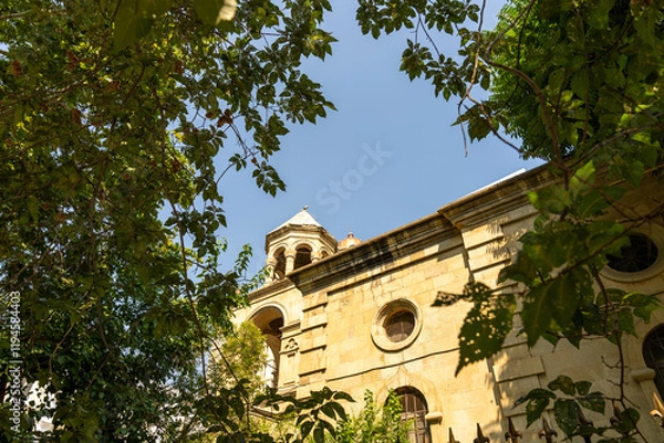 Fototapeta A church with a tall steeple and a large window. The building is surrounded by trees and the sky is clear