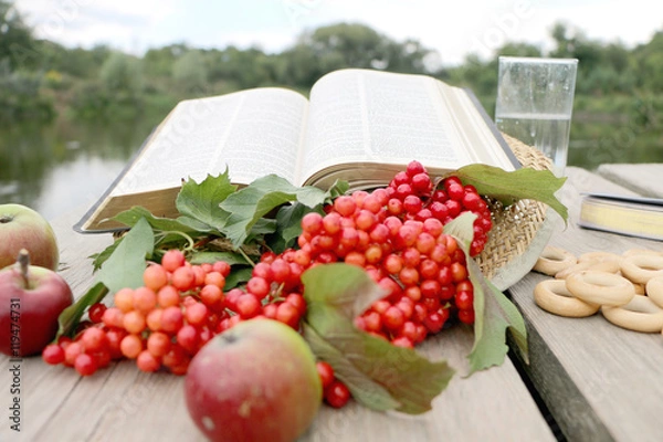 Obraz Red berries viburnum , green apples,bagels, a glass with  water in it wooden background and river with blue clouds in it