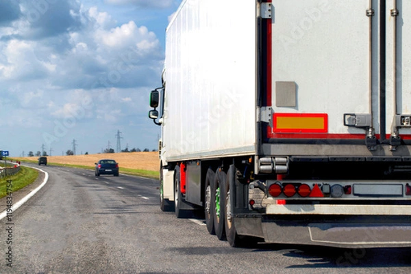Fototapeta A beautiful truck transports cargo along the highway in the summer. Concept of a cargo transport company. Work and vacancies as a freight forwarder driver. Copy space for text