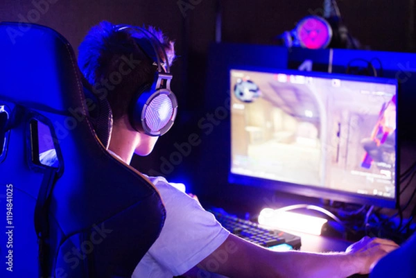 Fototapeta Professional gamer is playing a computer game on PC at cyber club. Player is participating in E-sports competition at gaming cafe. Gamer playing tactical shooter game during cyber sport tournament