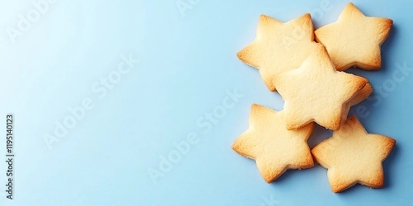 Fototapeta Star-shaped sugar cookies arranged on a light blue background with ample blank space for text on the left side of the image