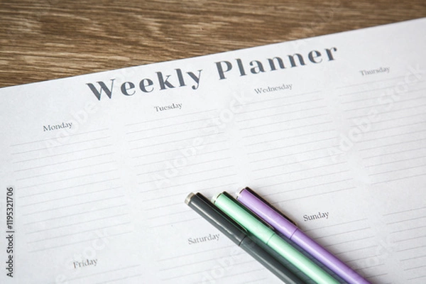 Fototapeta Weekly planner on a wooden desk with colorful pens ready for writing, concept of organization and productivity1