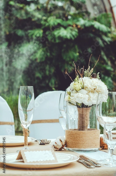Obraz Table set for an event party or wedding reception banquet. Winter bridal bouquet of white carnations flowers with twine in vase on craft background. wine glass, cutlery, napkin. Rustic style.