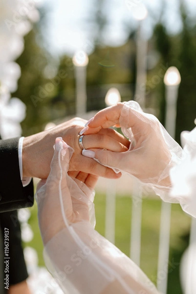 Obraz Wedding rings exchange. A bride and groom are getting married and exchanging rings. The bride is wearing a white dress and the groom is wearing a suit